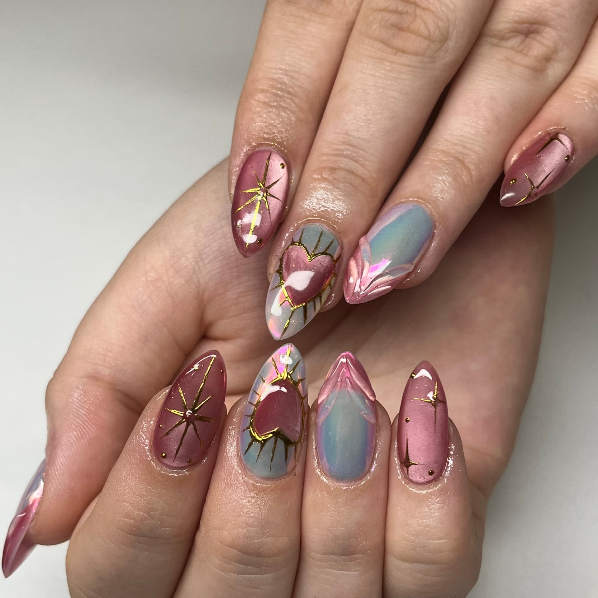 Almond nails in rose chrome and opal with hand-painted gold outlined hearts and starbursts