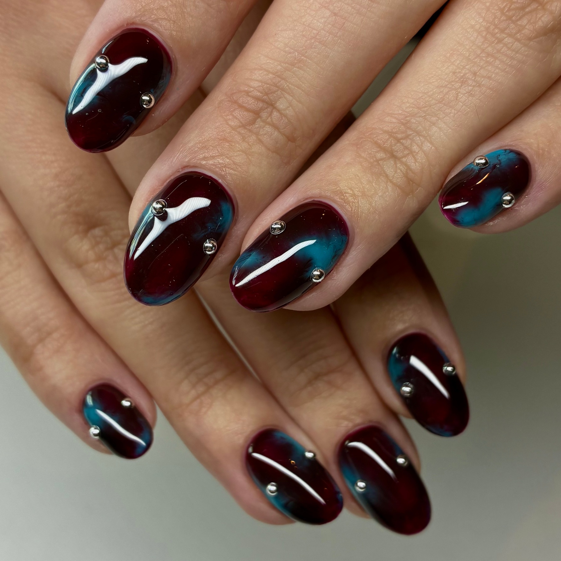 Burgundy and teal chrome nails with silver stud accents