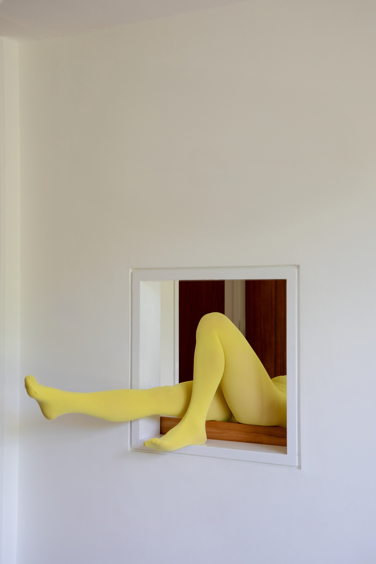 Legs in bright yellow tights stretched through a white wall frame, a playful nod to a water-free pedicure