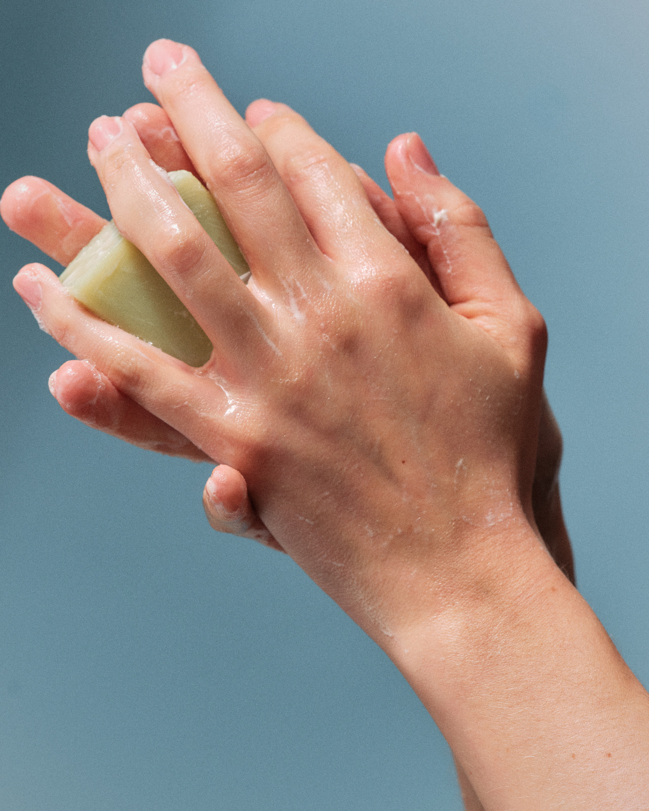 Hands washing with a plastic-free bar of soap against a blue background