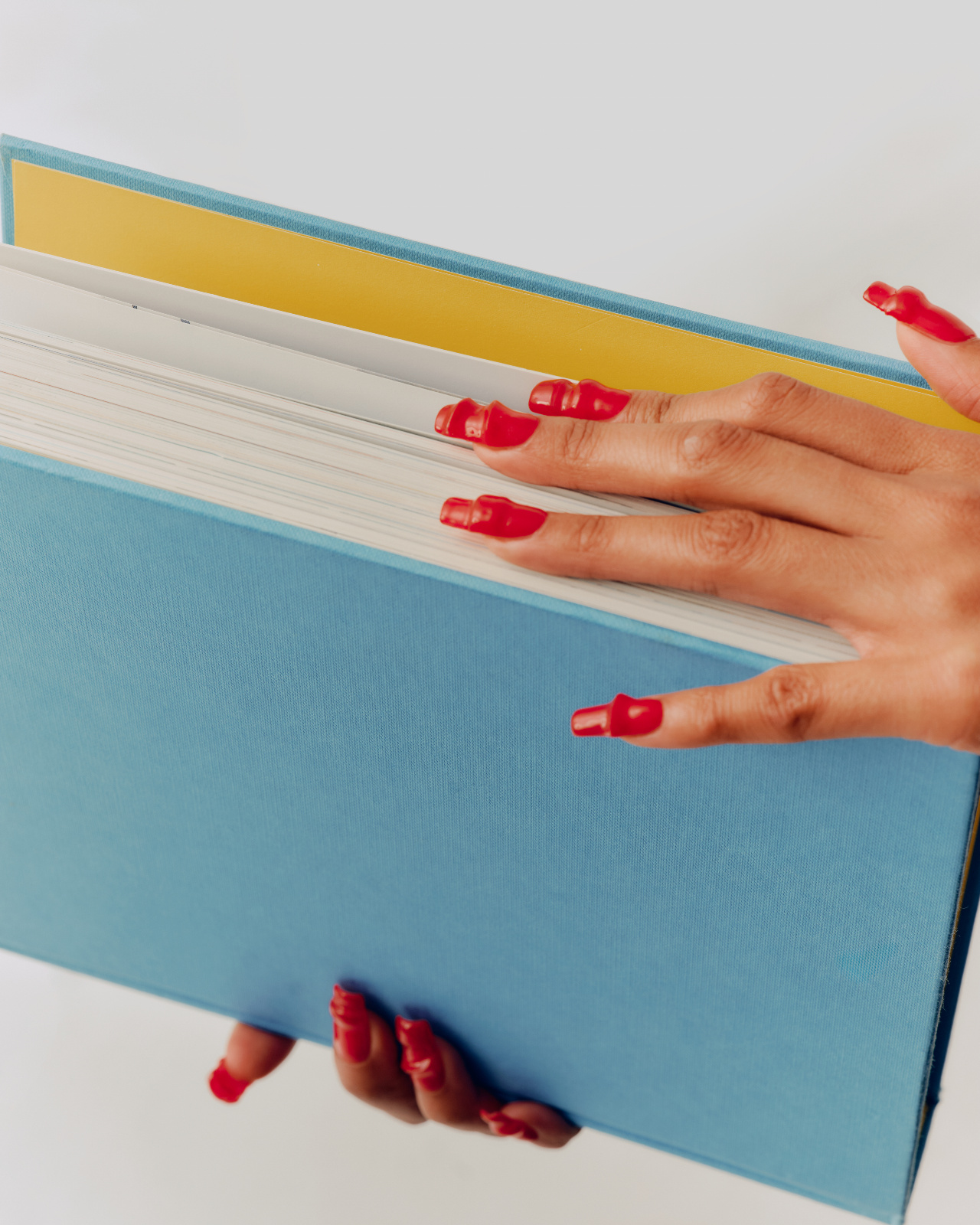 Long square red Gel-X extensions holding a blue hardcover book, glossy soft gel finish