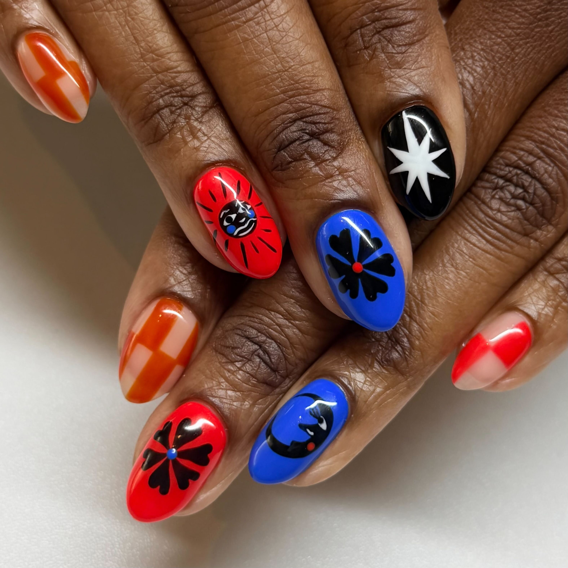 Almond nails in red, blue, orange and black with hand-painted folk art flowers, faces and stars